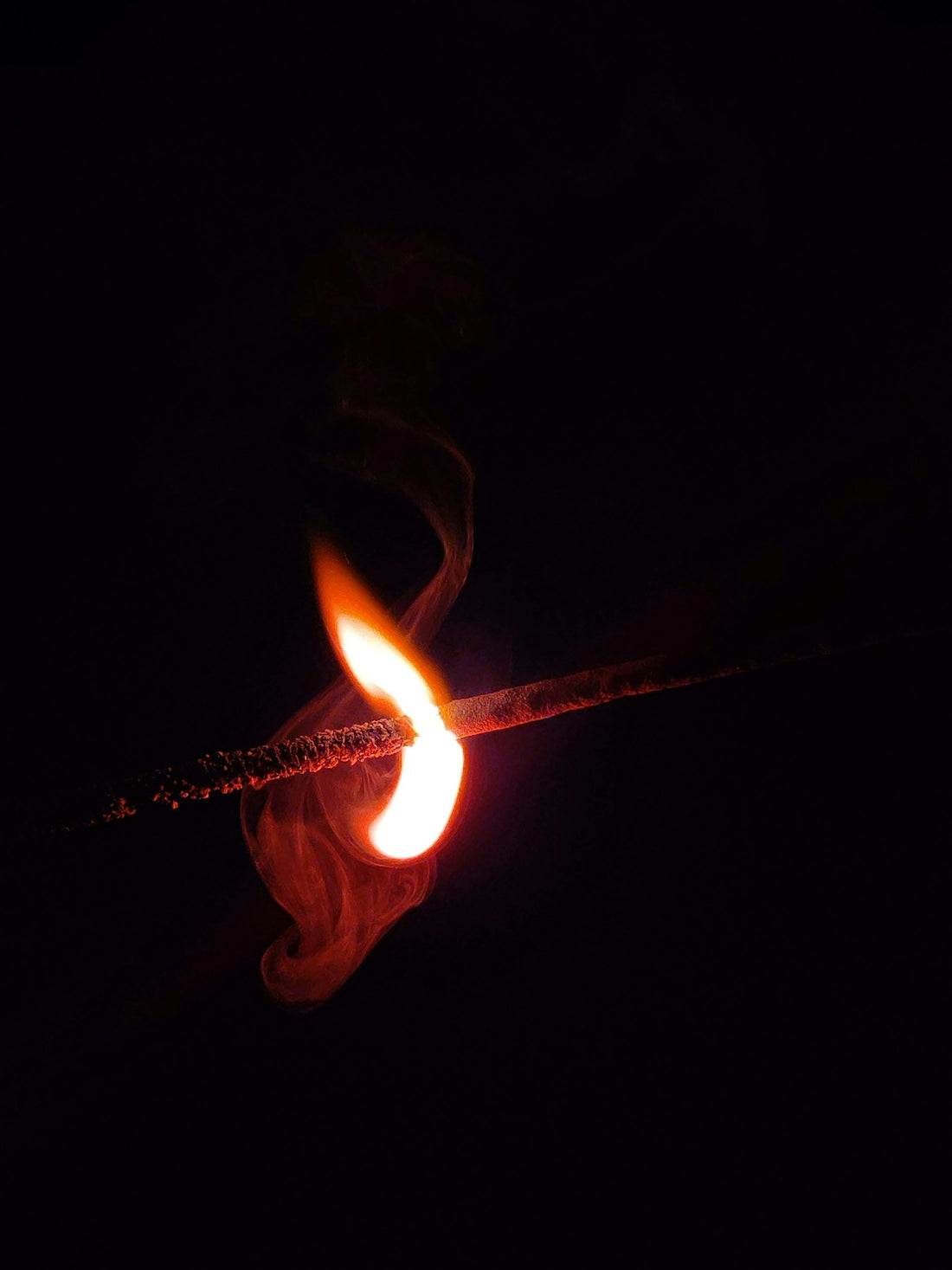 A lit matchstick in the dark with a red flame