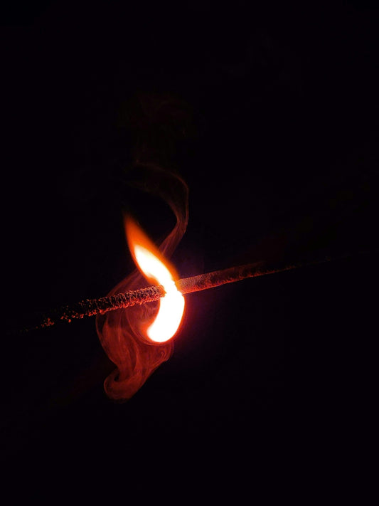 A lit matchstick in the dark with a red flame