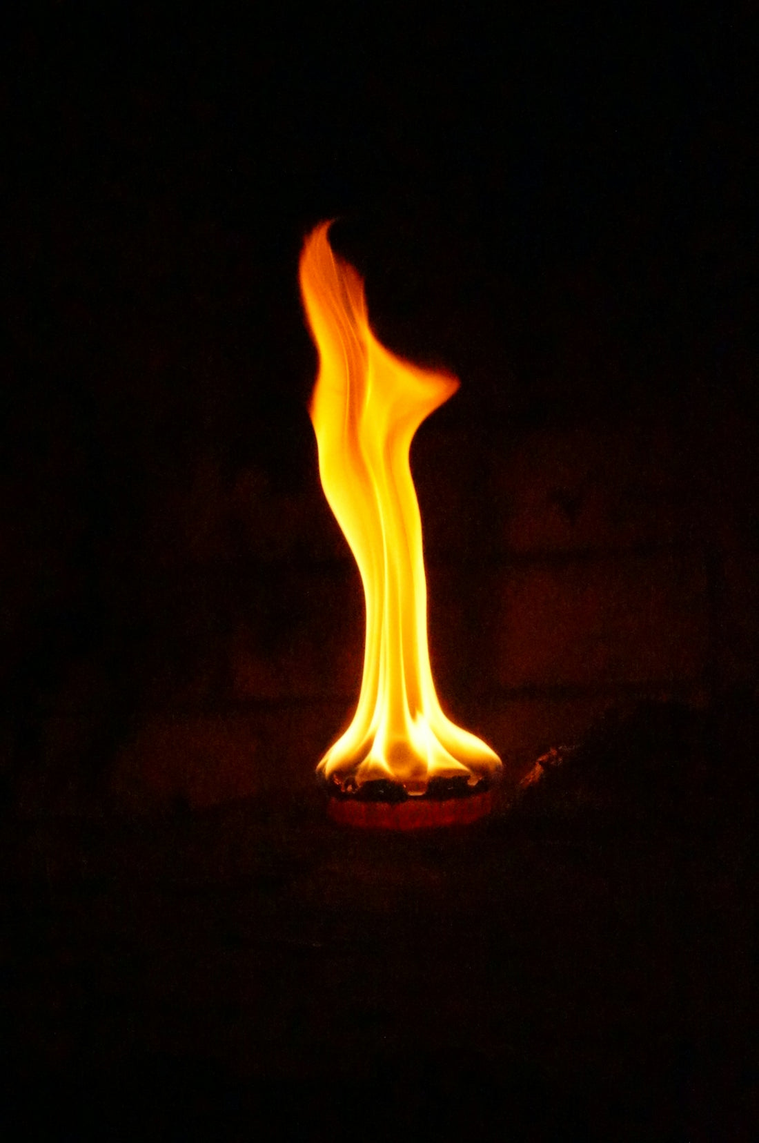A single flame burns brightly in the dark.